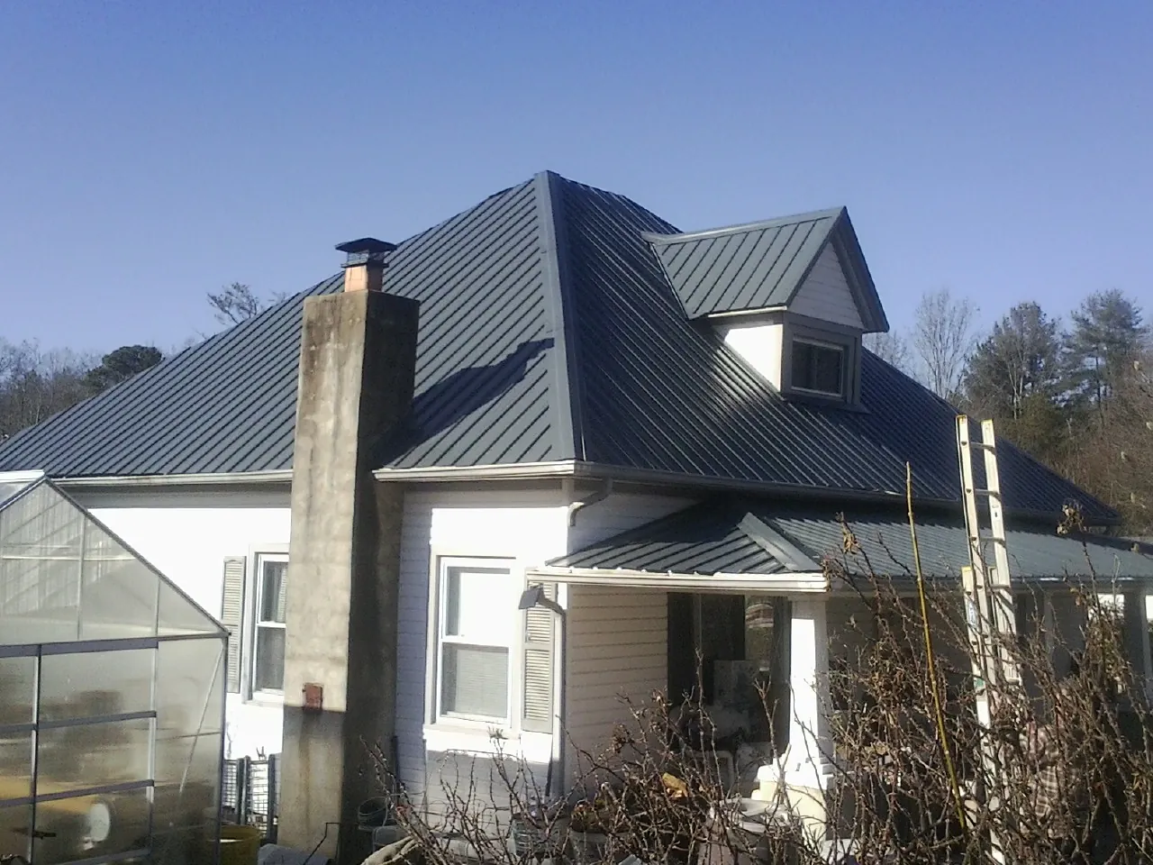Dark blue standing seam metal roof on a white farmhouse with dormer — Slate & Tile Roof Repair by Roofing Brothers in Brightwood