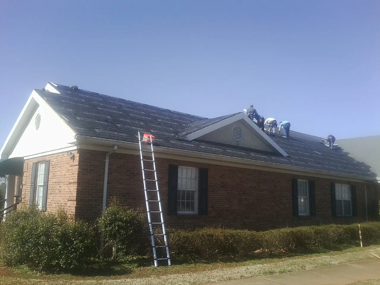 Crew tearing shingles off a brick ranch roof with a ladder set — Metal Roof Repair work by our crew in Brightwood
