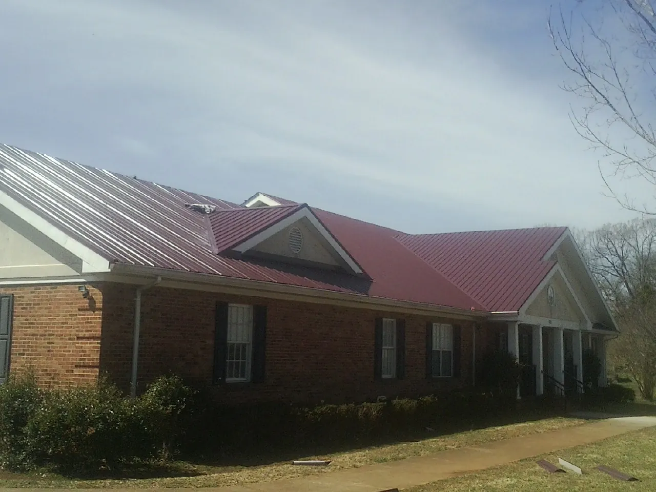 Red metal roof with gabled entries on a long brick building, from a Hail Damage Roof Repair job in Brightwood
