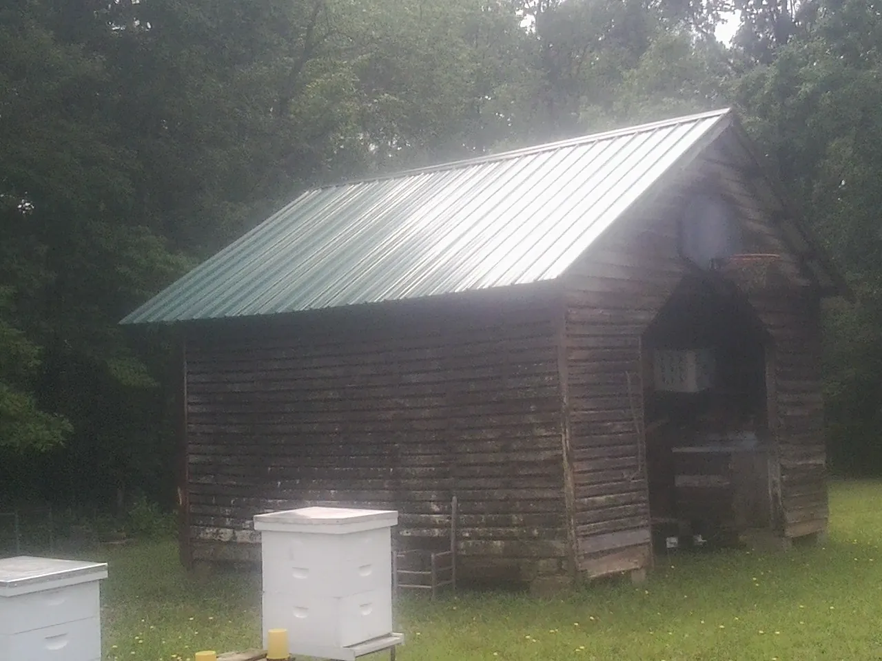 Green metal roof on a weathered barn beside stacked beehives in Brightwood