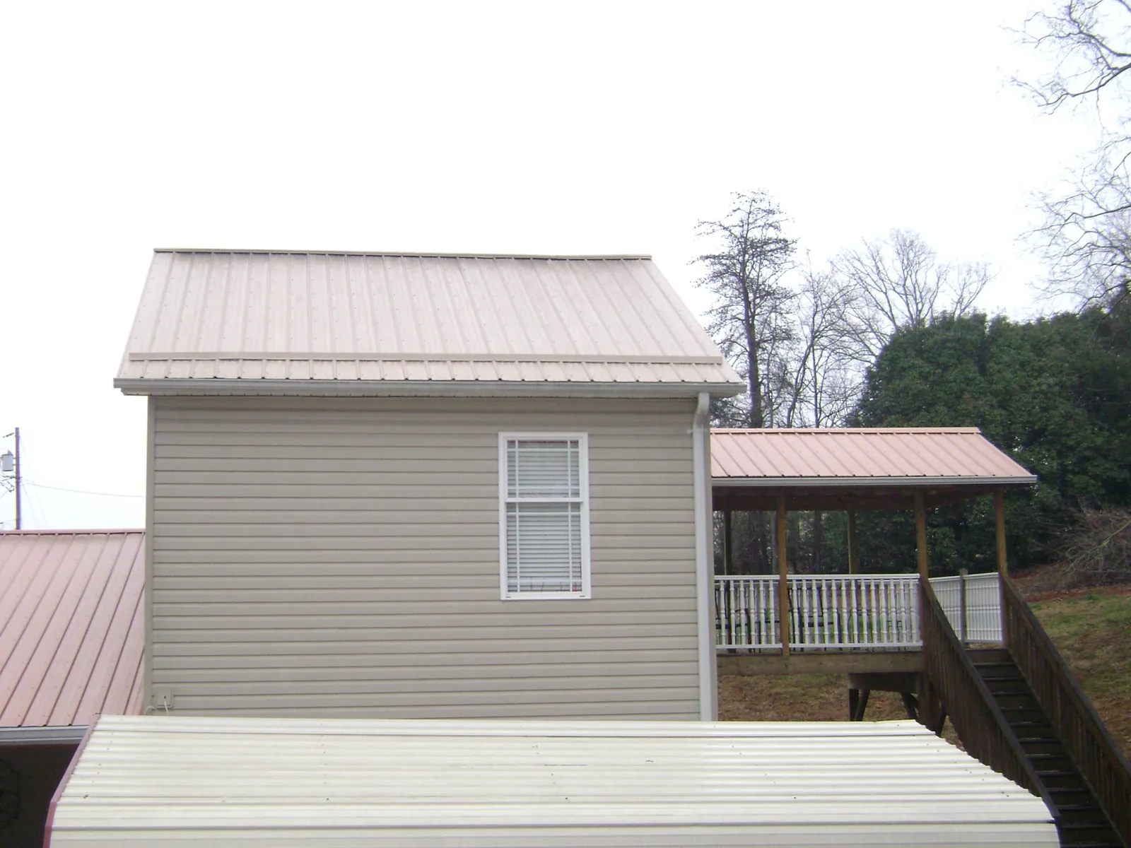 Tan metal roofs on a two story addition and attached porch, from a Roof Replacement job in Brightwood